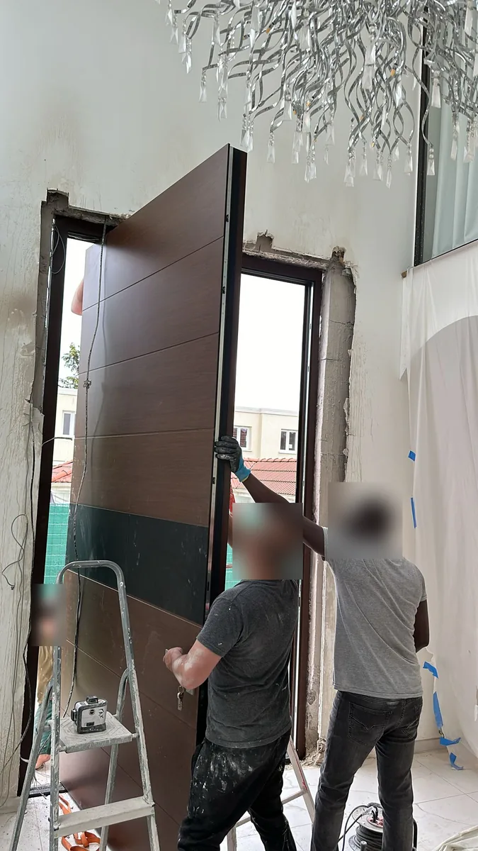Pose d’une porte d’entrée pivot décor bois et bande noire : trois poseurs présentent l’ouvrant sur son axe