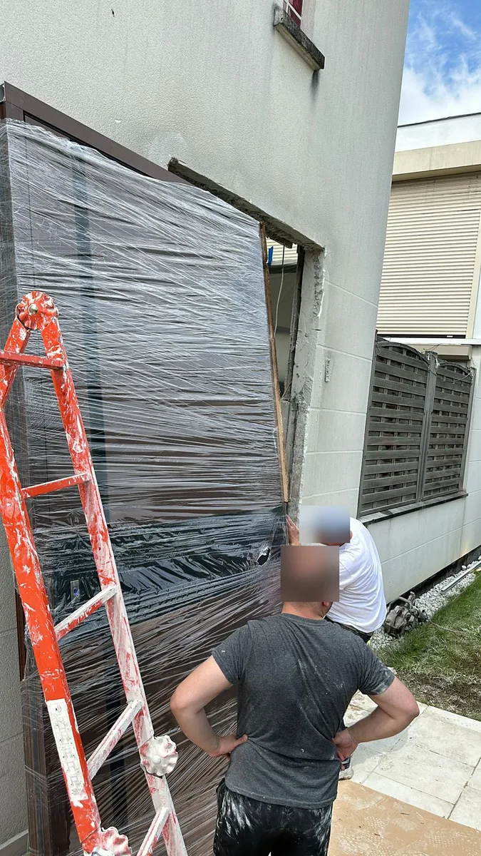 Porte pivot livrée sur chantier, encore filmée, devant la baie préparée