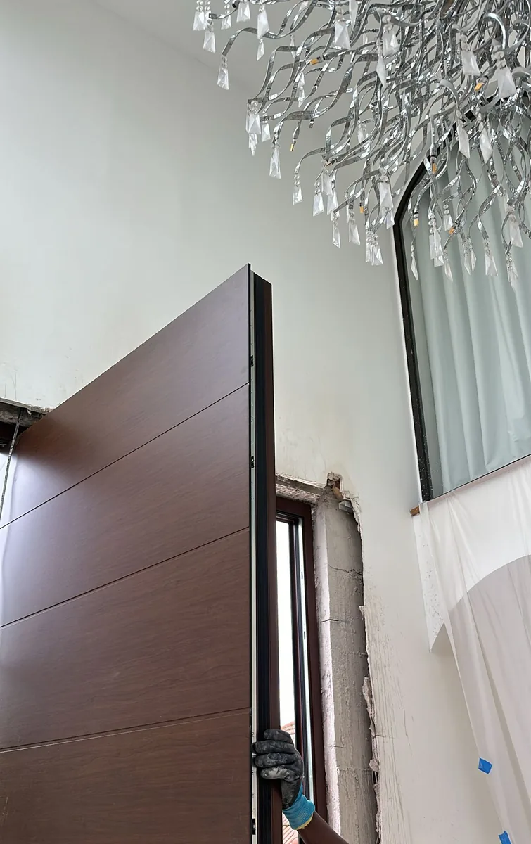 Mise en place de l’ouvrant d’une porte pivot de grande hauteur dans une entrée sous double hauteur