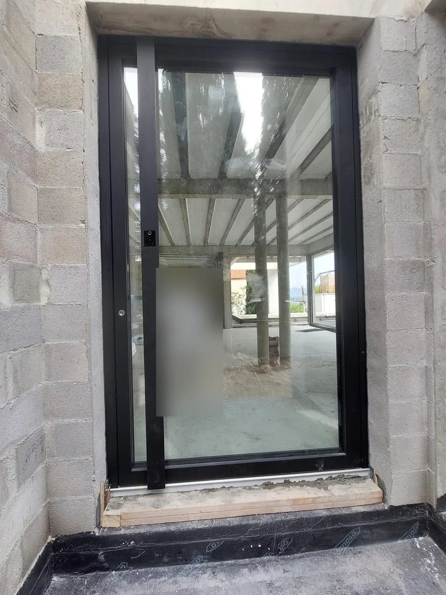 Porte pivot vitrée noire avec barre verticale, posée dans un mur en parpaings